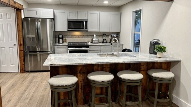 A modern kitchen with stainless steel appliances, a marble island with bar stools, and wooden beams on the ceiling.