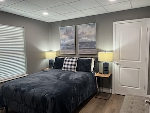 A bedroom with a bed, two wall-mounted lamps, a door, and a window with blinds.