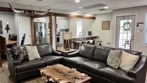 A modern living room with a leather sectional sofa, a coffee table with a fur throw, and a kitchen in the background.