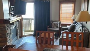 A living room with a wooden dining table, two chairs, a sofa, and a TV mounted on the wall.