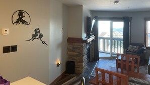 A living room with a stone fireplace, a dining area with wooden furniture, and a balcony with a view.