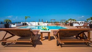 A poolside area with lounge chairs, a table, and a view of the ocean. - LUX 2BR Condo w/ Pool+ocean Views! Steps to Beach! (Playa del Carmen)