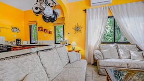 A living room with a sofa and armchair, a kitchen area, and a dining table. - Two Condos Next to Golf in Playacar!4br! Sleeps 12 (Playa del Carmen)