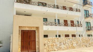 A multi-story building with balconies, a stone wall, and a wooden gate.
