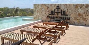A poolside area with lounge chairs and a stone wall with the name "TRINITY TULUM". - NEW Luxe Relaxing Loft ! Pool & Gym !! (Tulum)