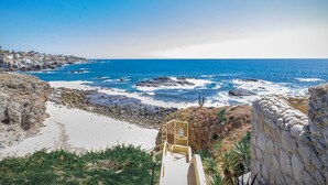 A coastal view with a rocky beach, a wooden staircase leading down to the shore, and a clear blue sky. - Stunning Pool & Ocean Views! Ground Floor Unit! (Cabo San Lucas)