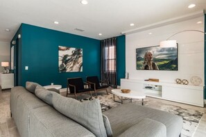 Ein modernes Wohnzimmer mit türkisfarbenen Wänden, einem grauen Sofa, einer weißen Unterhaltungsecke und einem großen Fernseher.