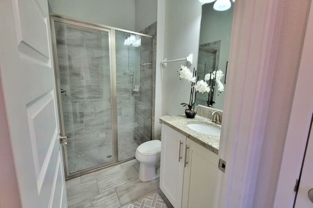 Ein modernes Badezimmer mit Duschkabine aus Glas, einer weißen Toilette und einem Waschtisch mit Spiegel und Orchidee im Topf.