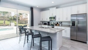 Une cuisine moderne avec des meubles blancs, un réfrigérateur en acier inoxydable et un grand îlot central doté de tabourets de bar.