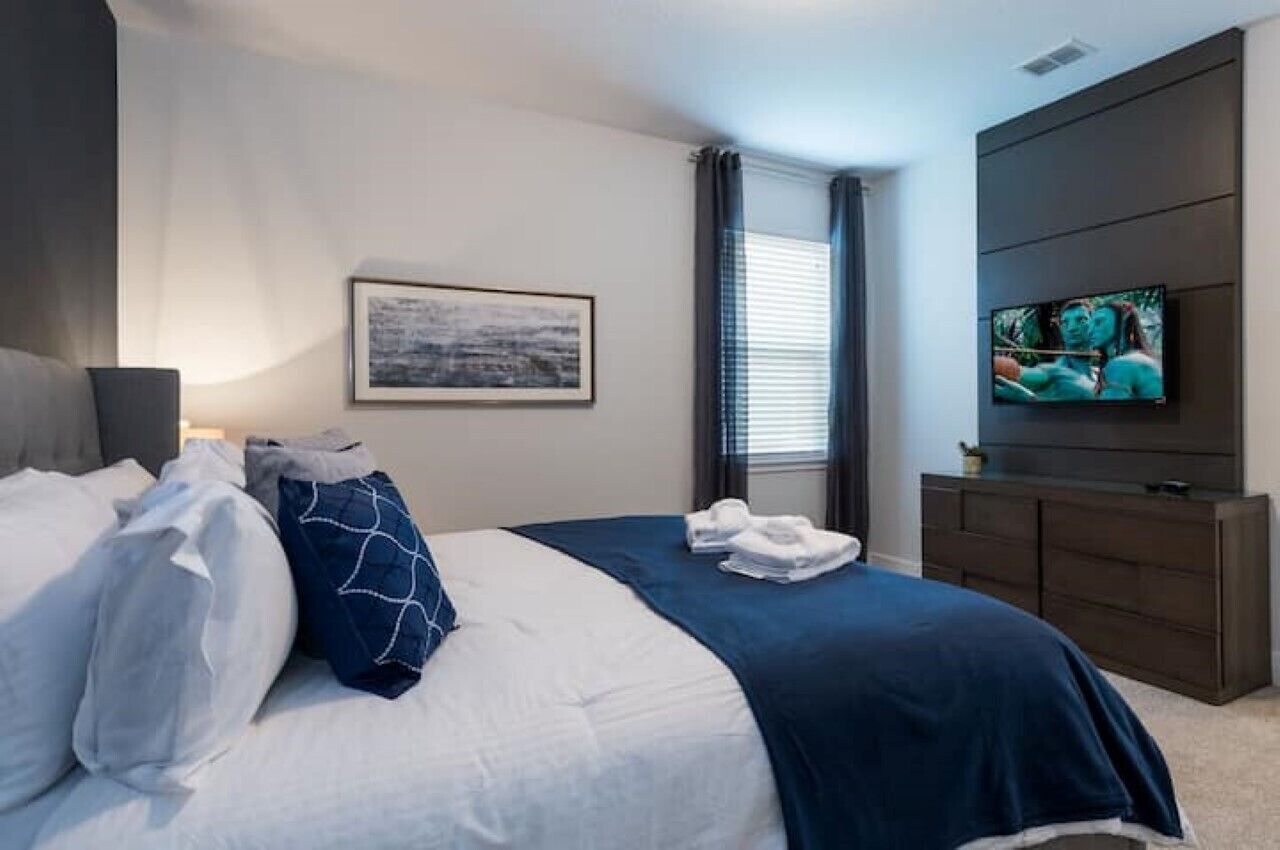 Une chambre d’hôtel avec un lit, un téléviseur à écran plat, un tableau au mur et une fenêtre avec des rideaux.