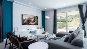 Un salon moderne doté d’un grand téléviseur à écran plat fixé au mur, d’un canapé, d’une table basse et d’un coin repas avec des chaises.