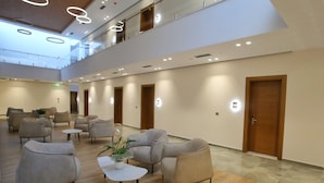 A spacious lobby with multiple seating areas, a central plant, and a high ceiling with circular light fixtures. - Portik Hotel (Berat)