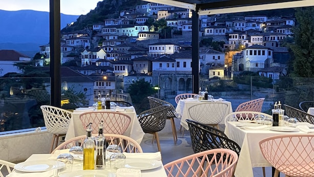 A restaurant with tables set for dining, featuring a view of a hillside town. - Portik Hotel (Berat)