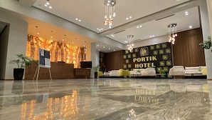 A spacious lobby with a polished marble floor, a reception desk, and a wall with the text "PORTIK HOTEL". - Portik Hotel (Berat)