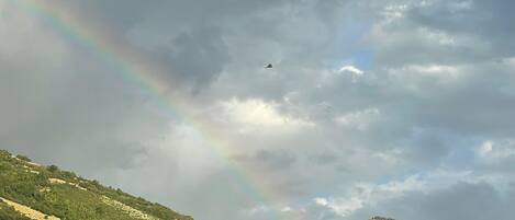 Un paysage de montagne avec un arc-en-ciel et un avion dans le ciel.