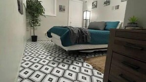 A bedroom with a patterned floor, a bed with a teal cover, a dresser, and a potted plant. - Gorgeous 2 bedroom in little Bohemian Omaha (Omaha)