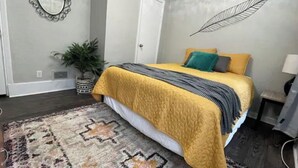 A bedroom with a bed, a patterned rug, a potted plant, and a wall decor piece. - Gorgeous 2 bedroom in little Bohemian Omaha (Omaha)