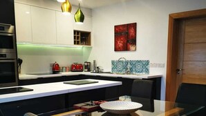 A modern kitchen with a glass dining table, black chairs, and pendant lights.