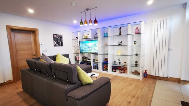 A modern living room with a dark brown sofa, a flat-screen TV, and a glass shelving unit with various decorative items.