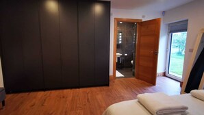 A bedroom with a large wardrobe, a bed with a white duvet, and a view of a bathroom and outdoor area through an open door.