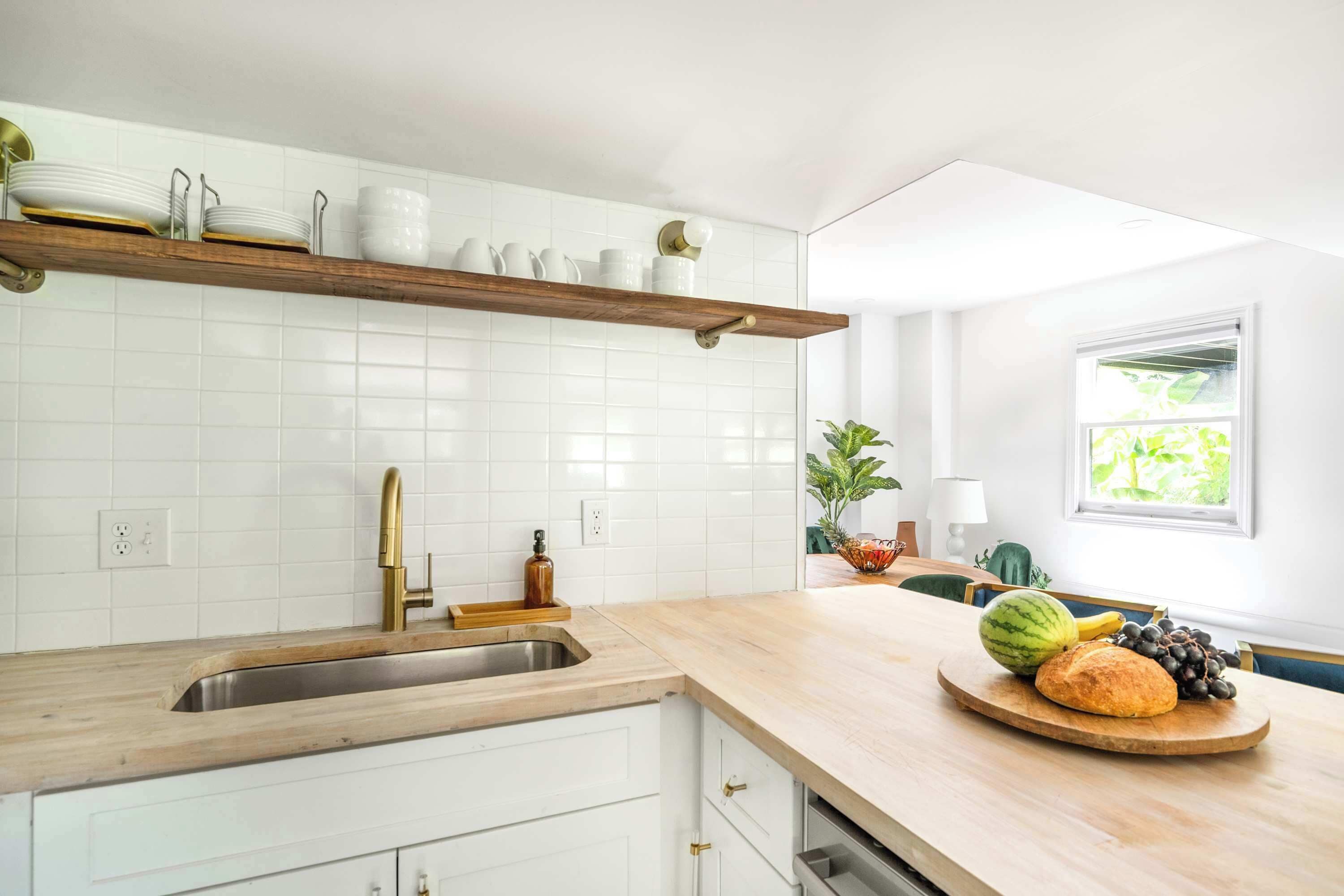 A kitchen with white cabinets, a wooden countertop, a built-in shelf with dishes, a sink, and a window with a view of greenery.