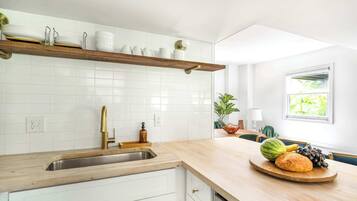 A kitchen with white cabinets, a wooden countertop, a built-in shelf with dishes, a sink, and a window with a view of greenery.