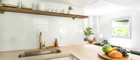 A kitchen with white cabinets, a wooden countertop, a built-in shelf with dishes, a sink, and a window with a view of greenery.