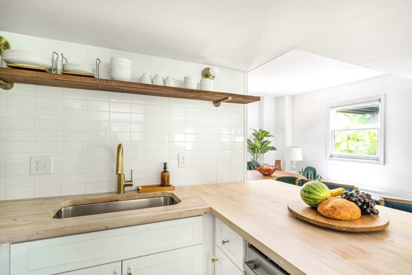 A kitchen with white cabinets, a wooden countertop, a built-in shelf with dishes, a sink, and a window with a view of greenery.