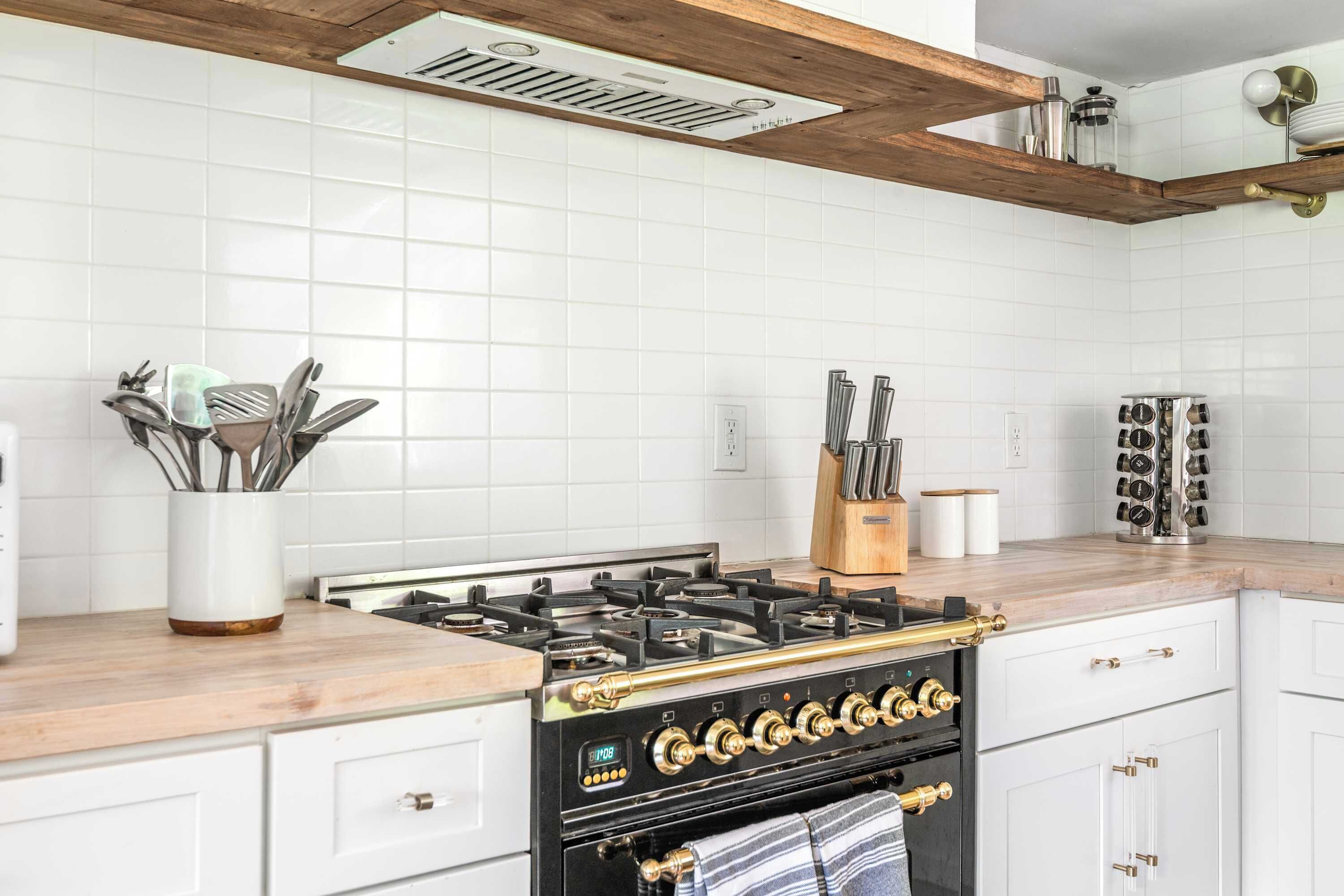 Une cuisine avec des carreaux blancs, une cuisinière à gaz et des poutres en bois au plafond.