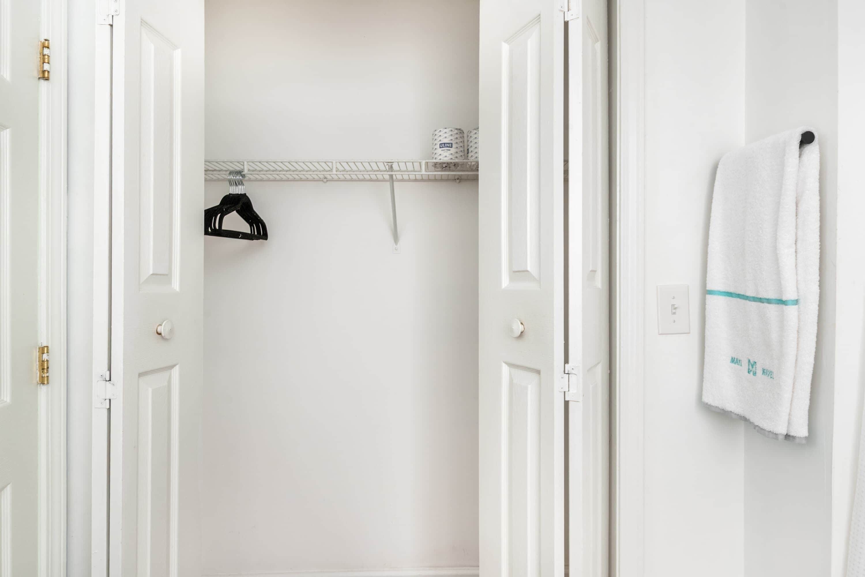 Une salle de bain blanche avec une serviette accrochée au mur, un porte-serviettes et une étagère contenant des articles de toilette.