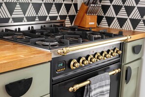 A kitchen with a gas stove, a clock displaying 2:47, and a knife block on the counter.