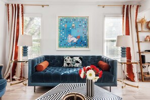 A living room with a blue sofa, two side tables with lamps, a patterned rug, and a framed artwork on the wall. - Brooklyn Bungalow (Atlanta)