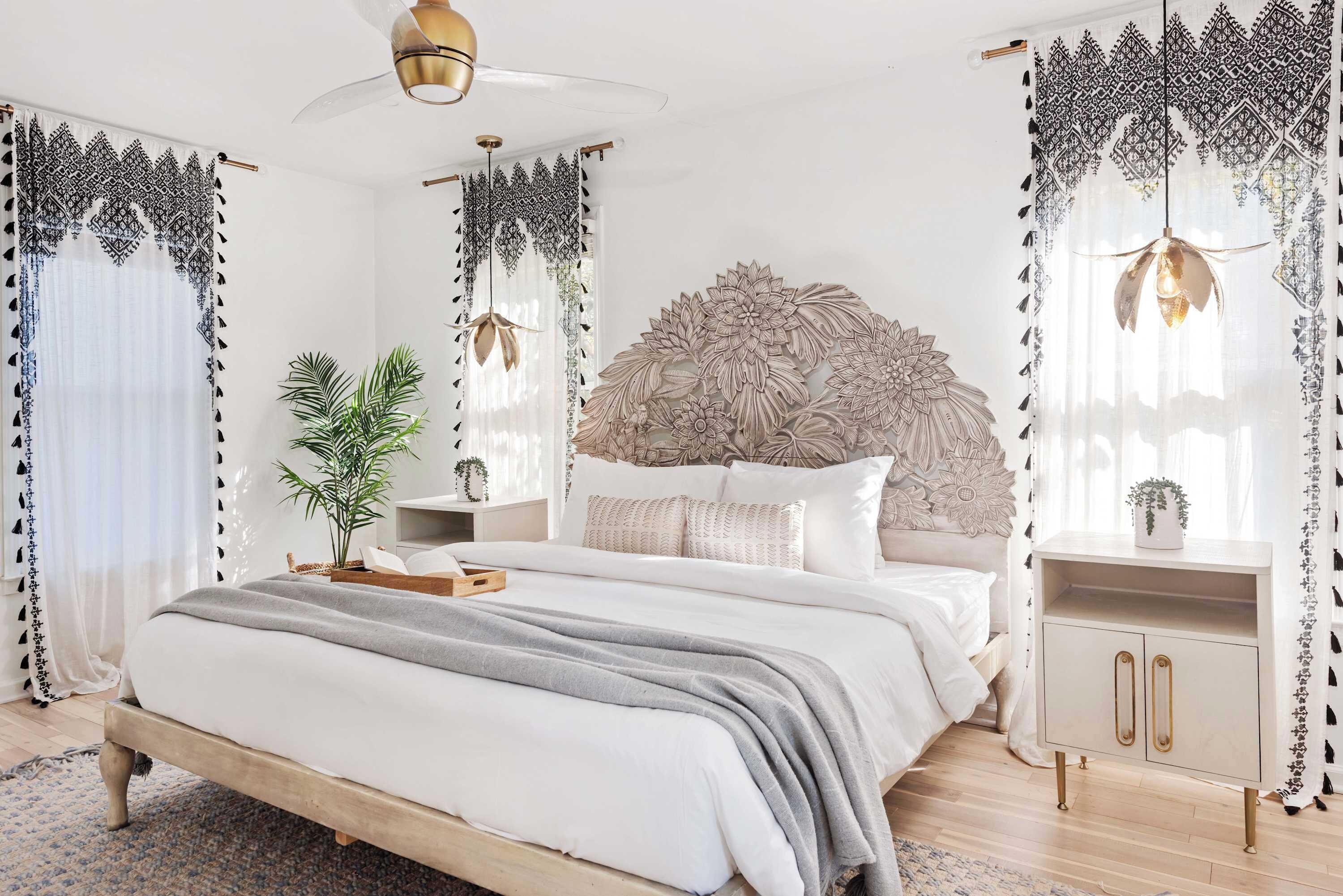 Une chambre à coucher comprenant un lit, des tables de chevet, une tête de lit décorative, des rideaux et un luminaire suspendu.