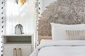 A bedroom with a bed, a nightstand, a window with curtains, and a wall with a floral design. - Brooklyn Bungalow (Atlanta)