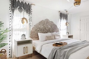 A bedroom with a large bed, a decorative headboard, a bedside table, and a hanging light fixture.