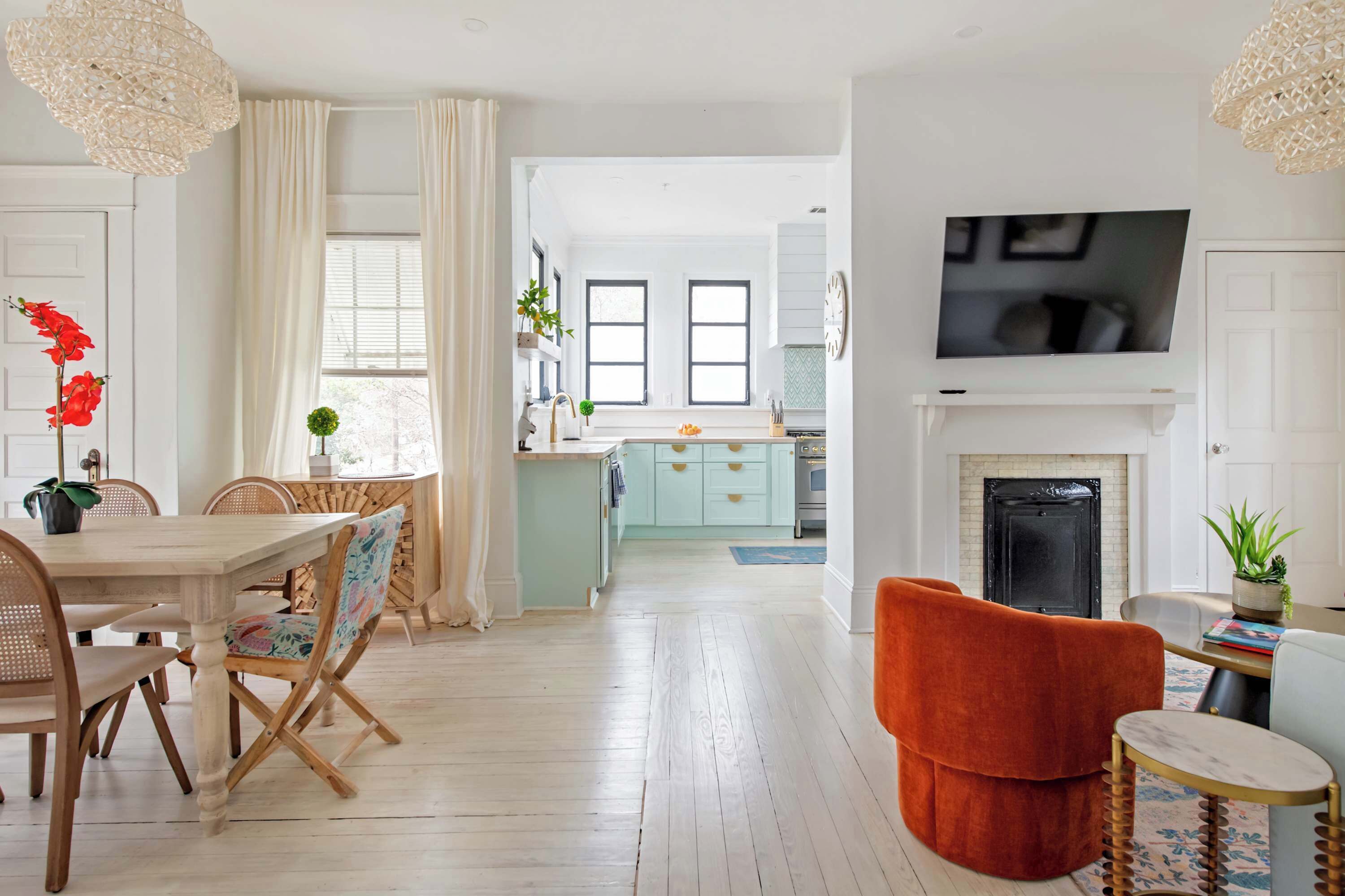 A spacious living room with a fireplace, a dining area with a wooden table and chairs, and a kitchen in the background.