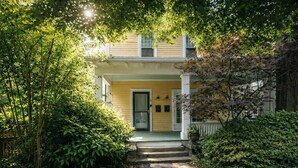 A two-story house with a front porch, surrounded by dense greenery.