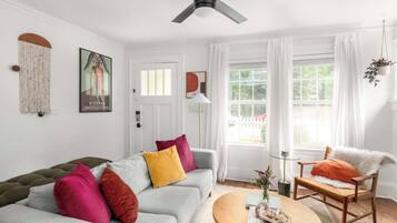 A living room with a grey sofa, colorful cushions, a wooden coffee table, and a ceiling fan.