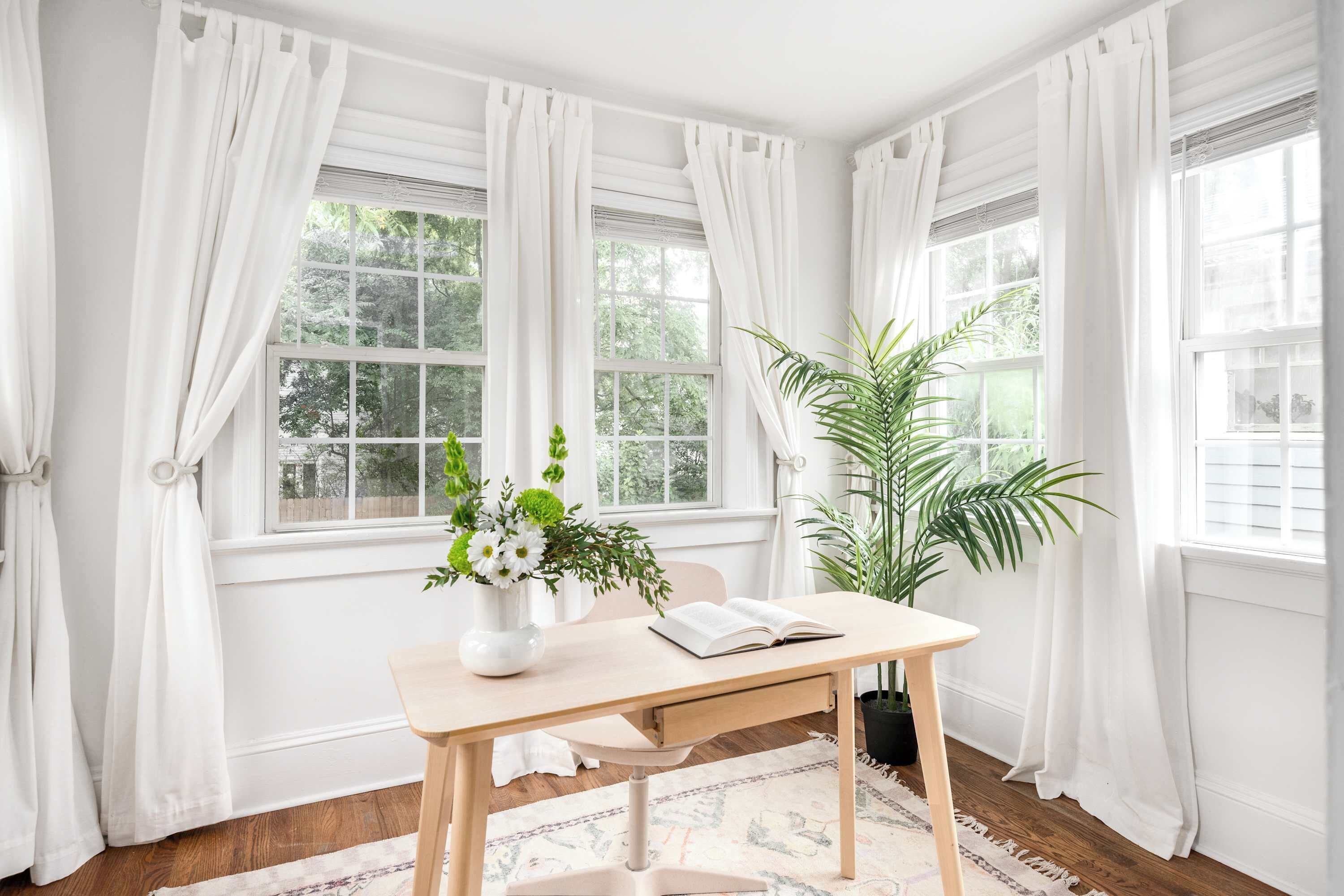 Quarto com escrivaninha de madeira, uma cadeira, um vaso com flores e uma planta em vaso.