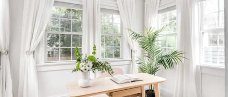 Ein Zimmer mit einem Holztisch, einem Stuhl, einer Vase mit Blumen und einem Blumentopf.