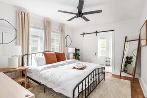 Un dormitorio con cama, mesitas de noche, ventilador de techo, espejo y ventana con cortinas.