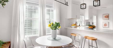 A modern kitchen with white cabinetry, a round white table, and two bar stools.