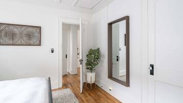 A bedroom with a bed, a large mirror, a potted plant, and a door leading to another room.