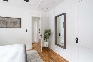 Une chambre à coucher avec un lit, un grand miroir, une plante en pot et une porte donnant sur une autre pièce.