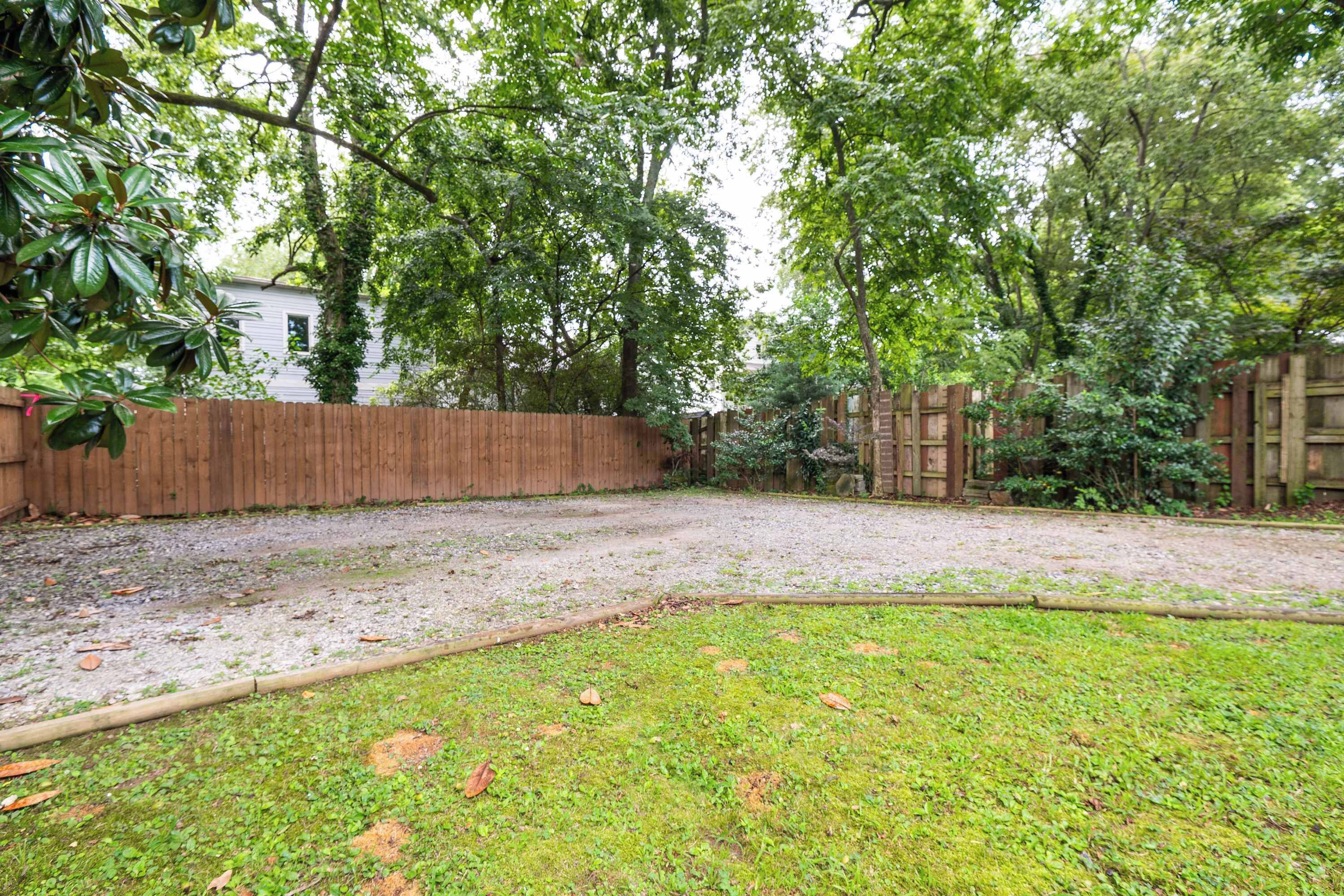 A backyard with a wooden fence, a grassy area, and trees.