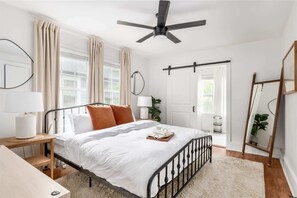 Une chambre à coucher comprenant un lit, des tables de chevet, un ventilateur de plafond et une grande fenêtre avec des rideaux.
