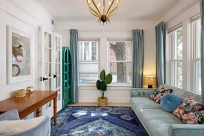A cozy living room with a blue patterned rug, a light blue sofa with floral cushions, a wooden side table, and a green arched bookshelf. - Moreblue (Atlanta)