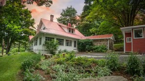 Une maison dotée d’un toit végétalisé, entourée d’un jardin où poussent différentes espèces de plantes, avec un grand rocher en premier plan.