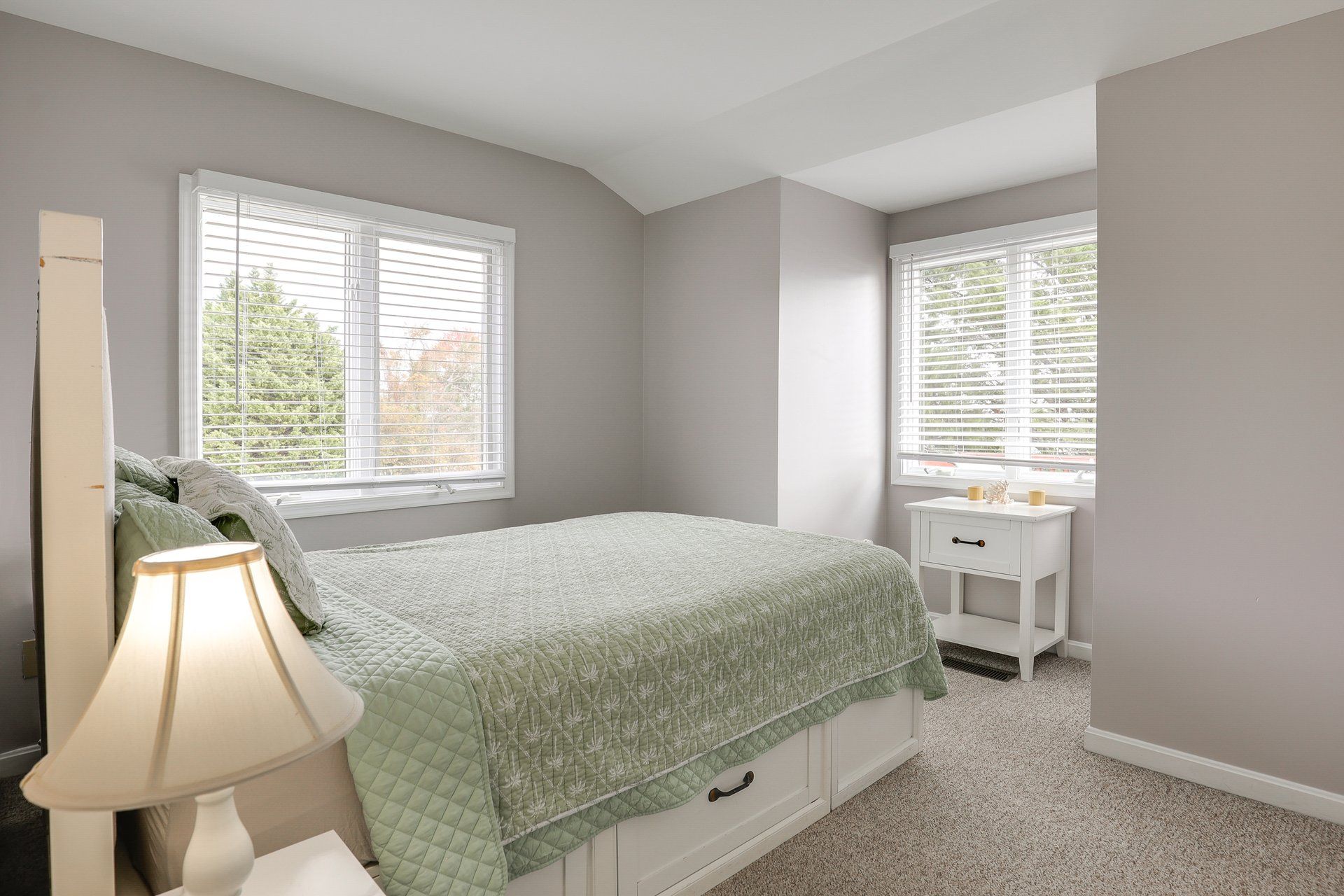 A bedroom with a bed, a nightstand, a lamp, and a window with blinds.