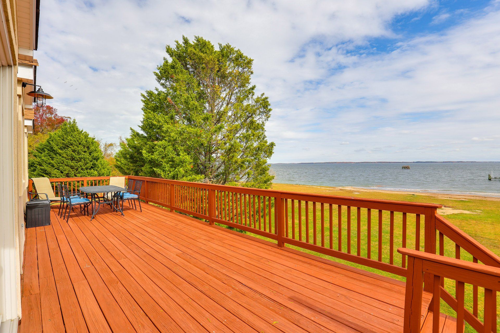 A wooden deck with outdoor furniture, a view of the water, and a tree.